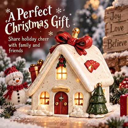 Christmas bow house styled among snowy greenery and wrapped gifts beside a snowman decoration and a festive wooden sign.